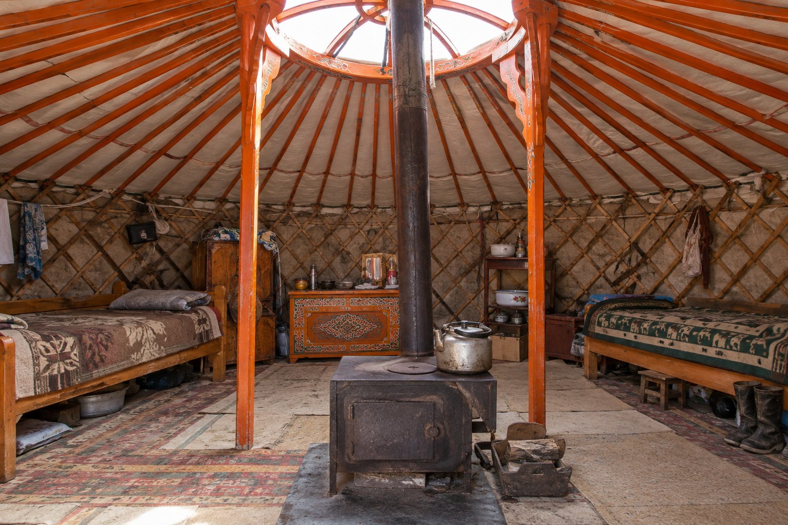 Interior of a Mongolian ger with beds, orange wooden roof poles and a central stove